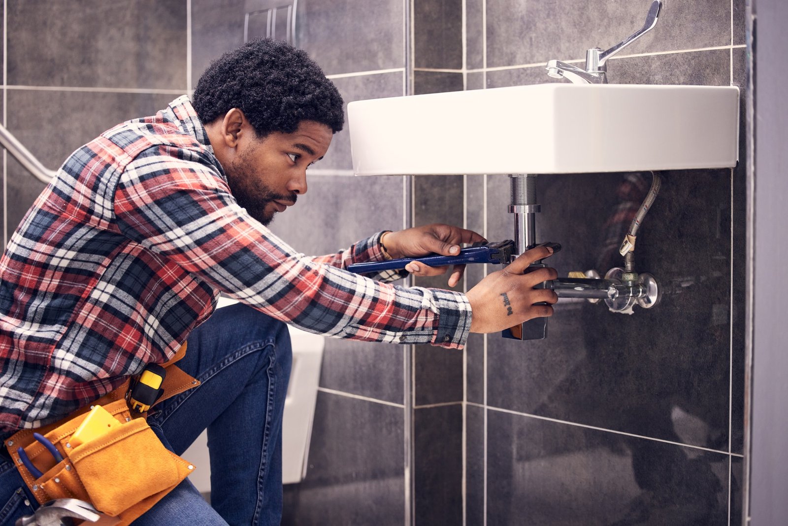 black-man-plumber-and-maintenance-in-bathroom-fixing-sink-pipe-with-wrench-and-plumbing-industry-.jpg